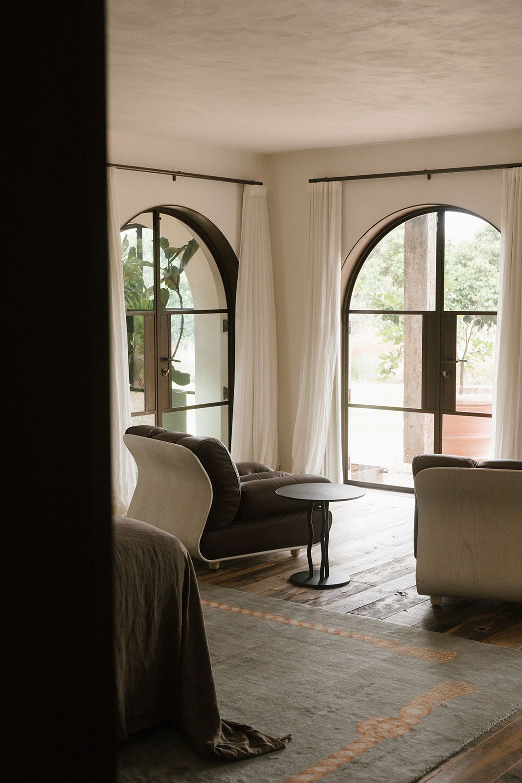 Elegant living room interior with arched windows, white curtains, and modern seating around a small side table.