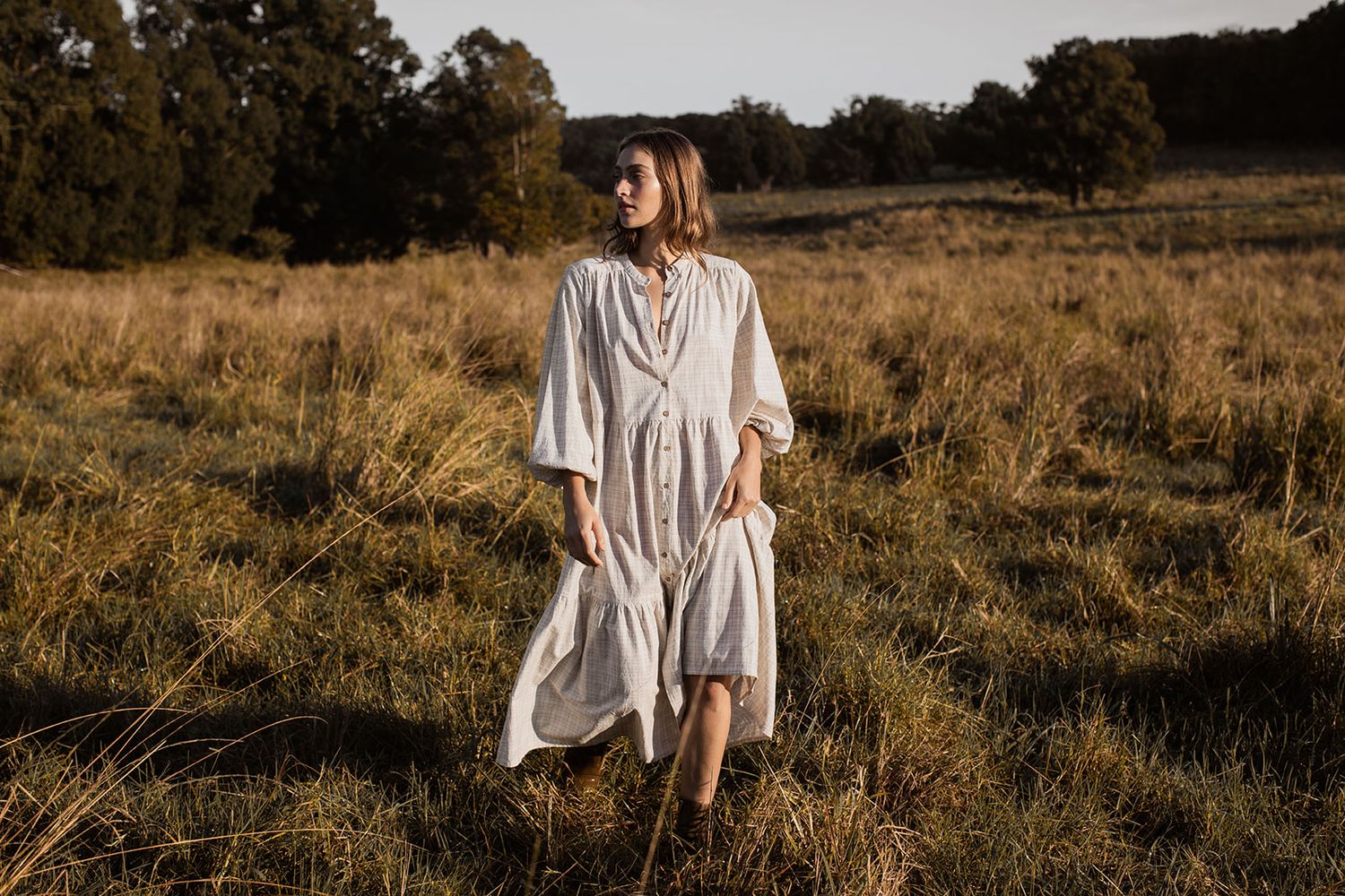Figure in white flowing dress walks through golden sunlit meadow at dusk creating dreamy ethereal scene.