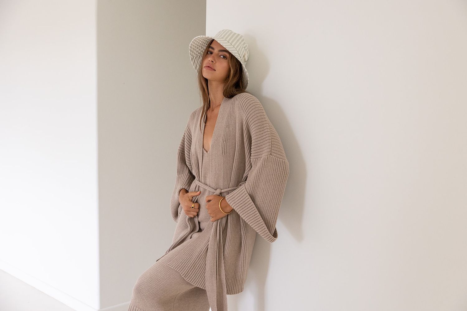 Woman in beige loungewear poses against white wall in a series of lifestyle photos.
