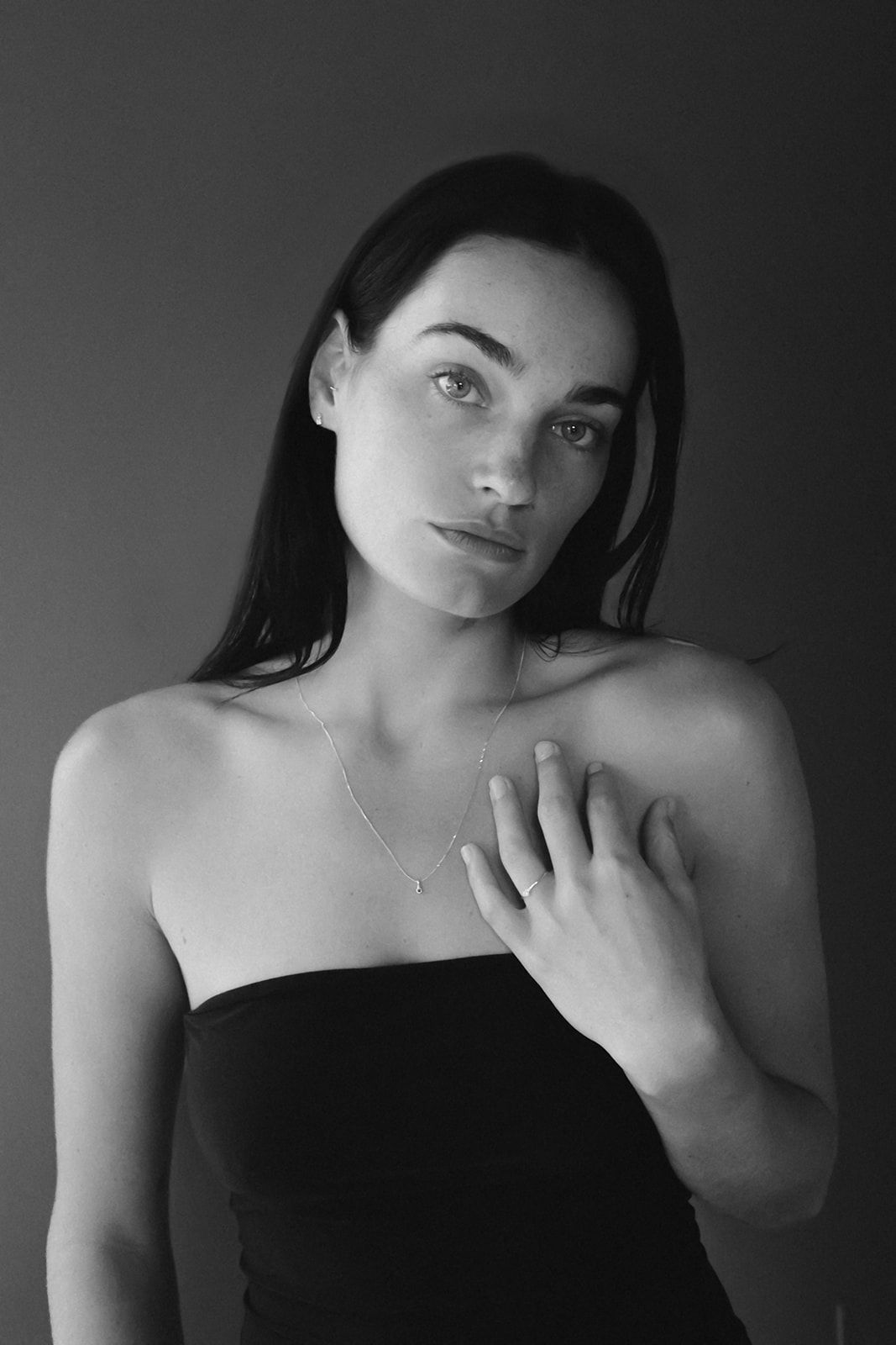 Black and white portrait photograph of someone in a strapless top with long dark hair against a simple background.