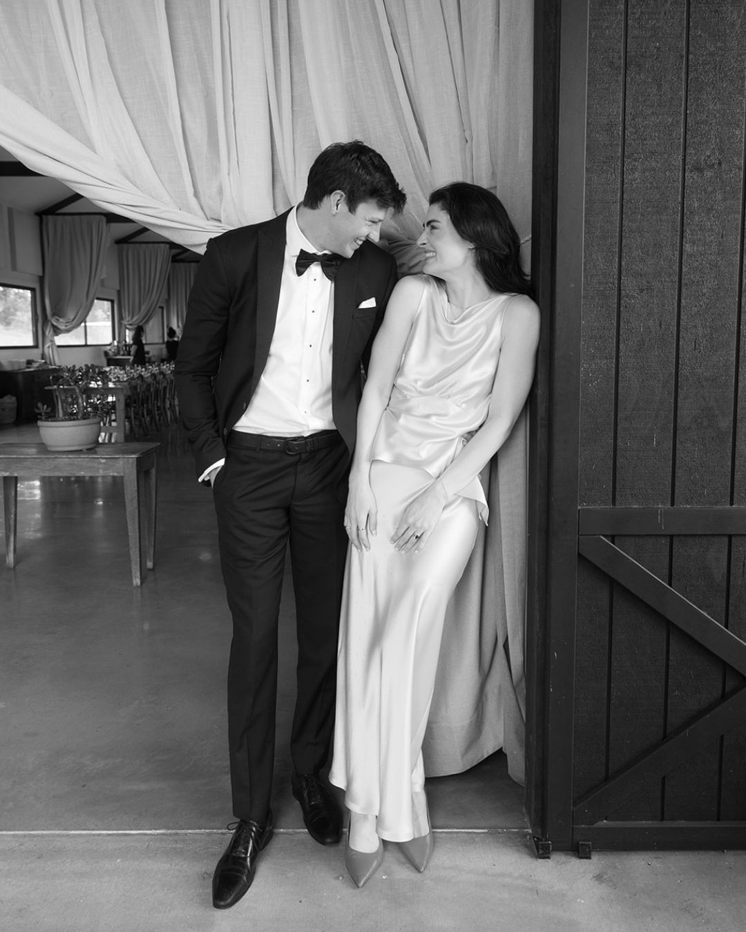 Black and white photo of an elegant couple in formal attire sharing a romantic moment in a doorway.