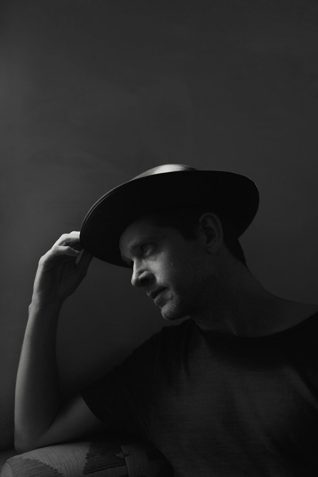 A dramatic black and white series of silhouettes showing a person adjusting their hat in moody lighting.