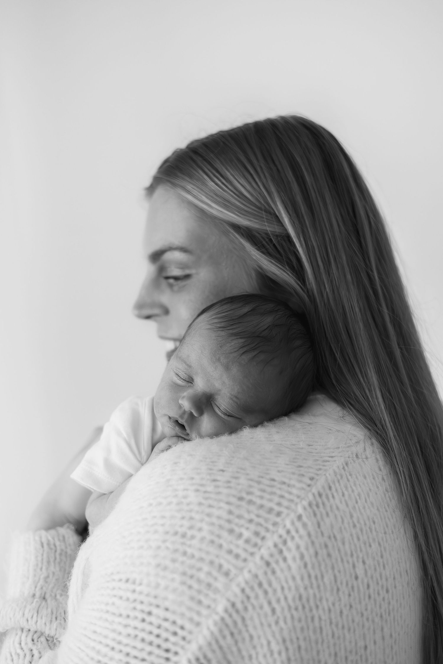 Black and white photo of a mother with long hair tenderly holding her sleeping newborn baby against her shoulder.