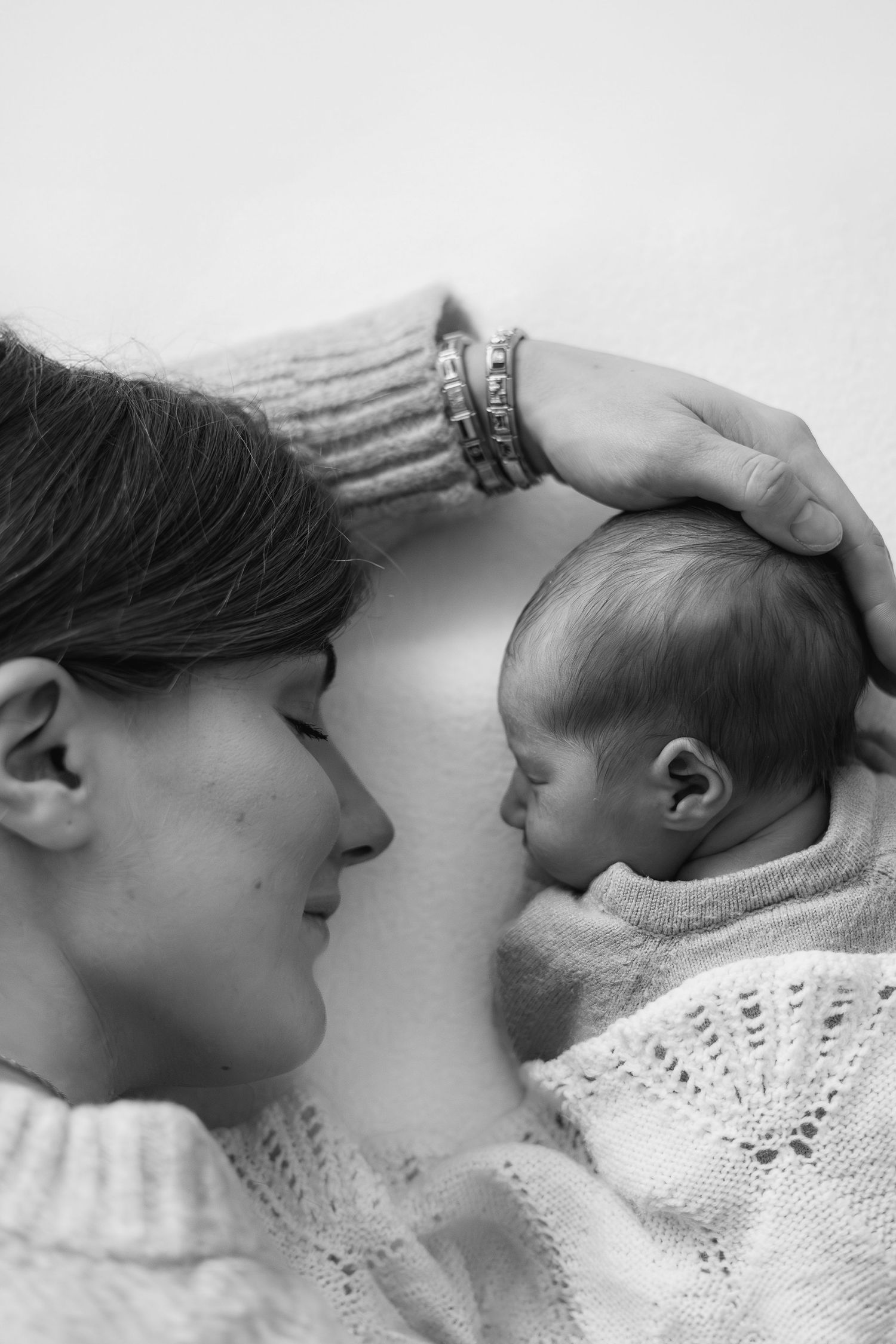 Black and white photo of a mother tenderly cradling her newborn baby, gently placing her hand on the infant's head.