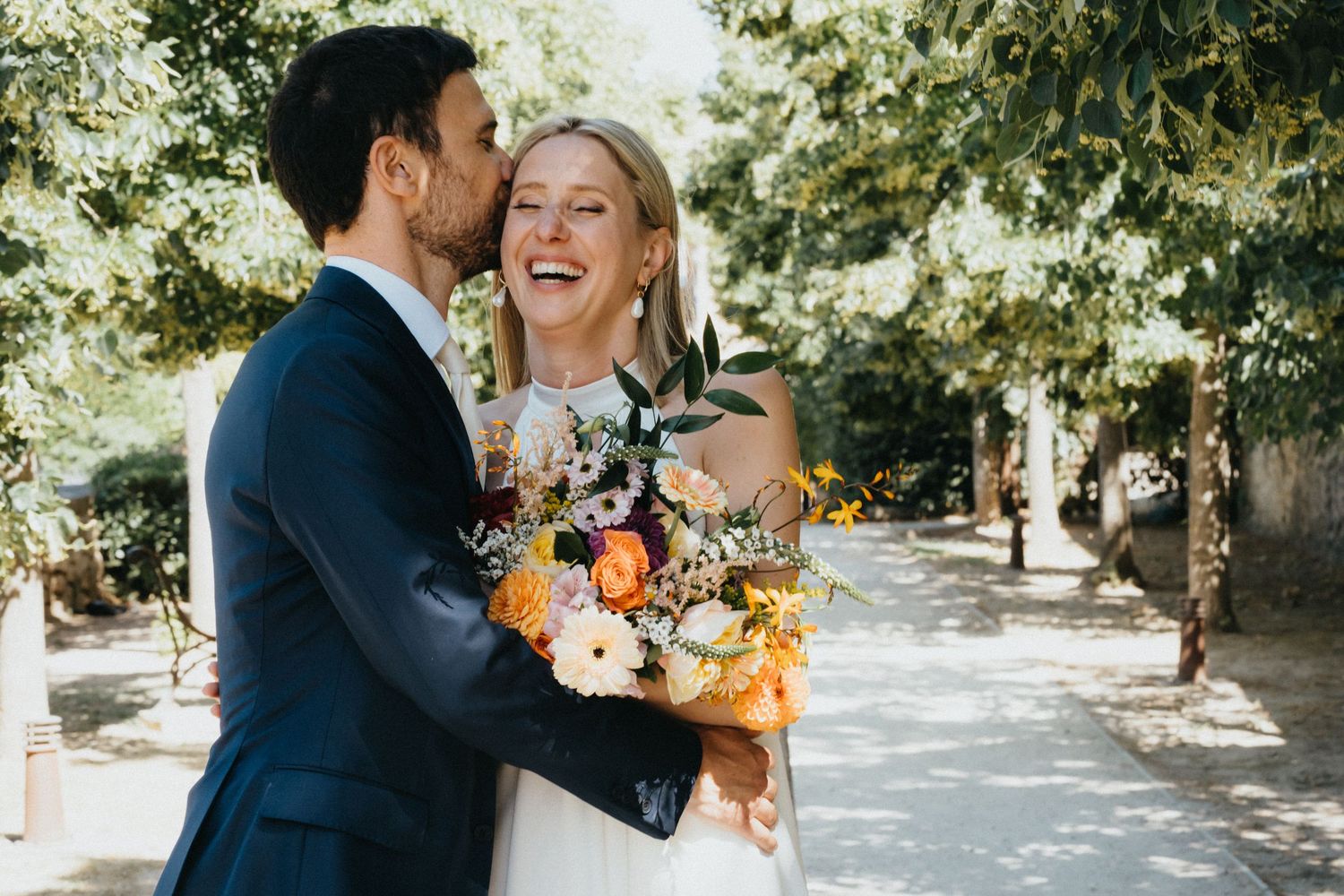 Couple de mariés qui rit en extérieur avec un bouquet de fleurs