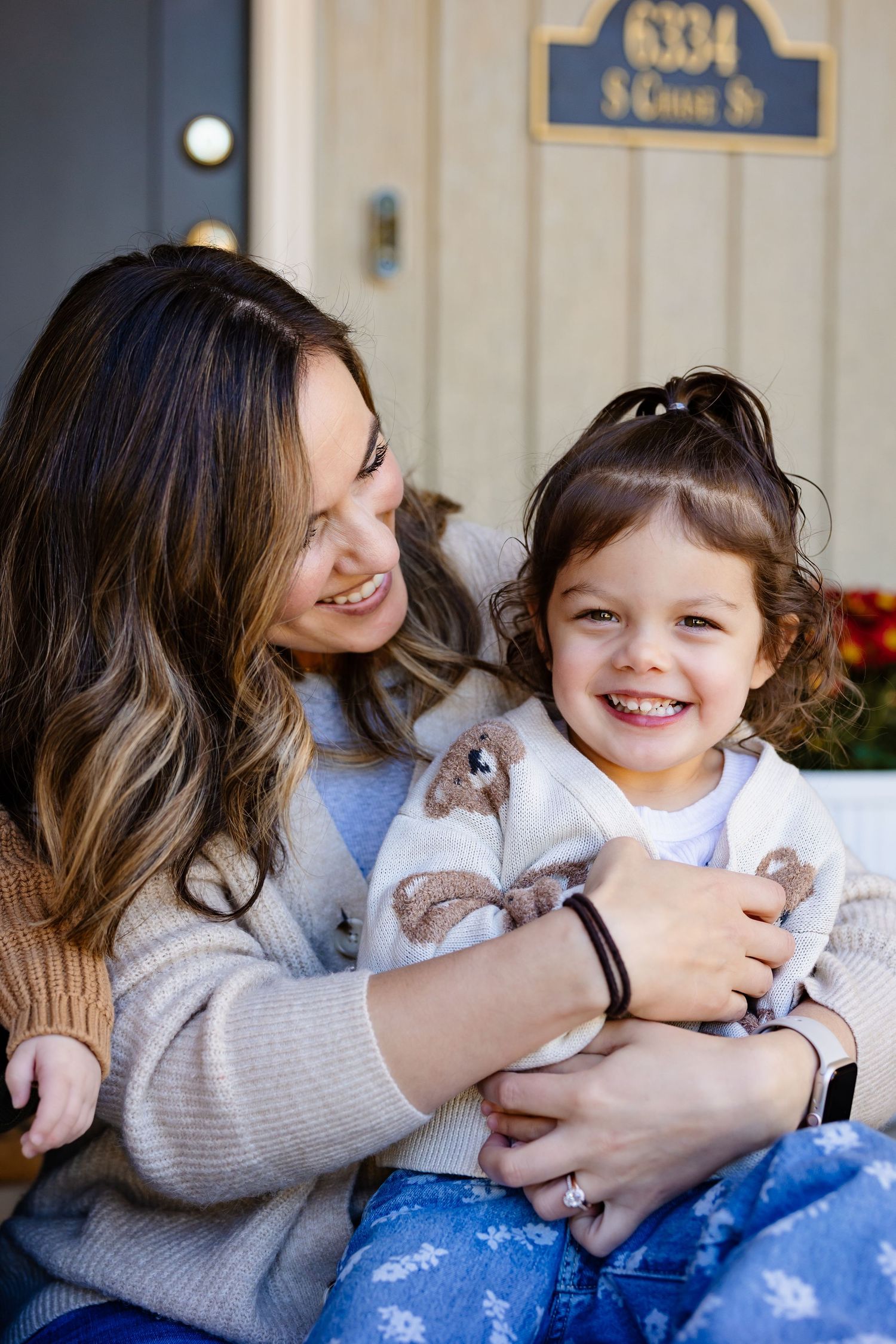 Smiling mother hugging her happy toddler daughter on a front porch steps outdoors.