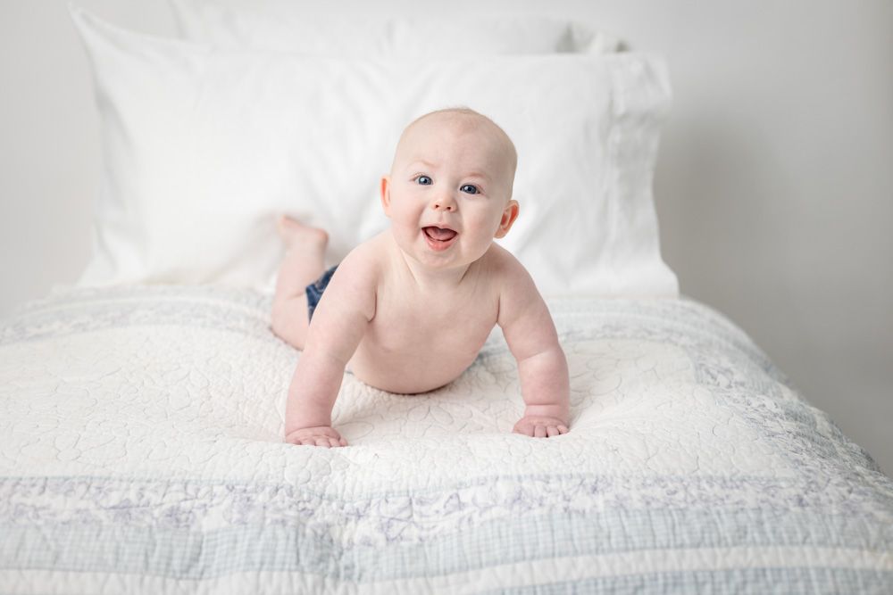 Baby boy crawls on white bedding during photography session.