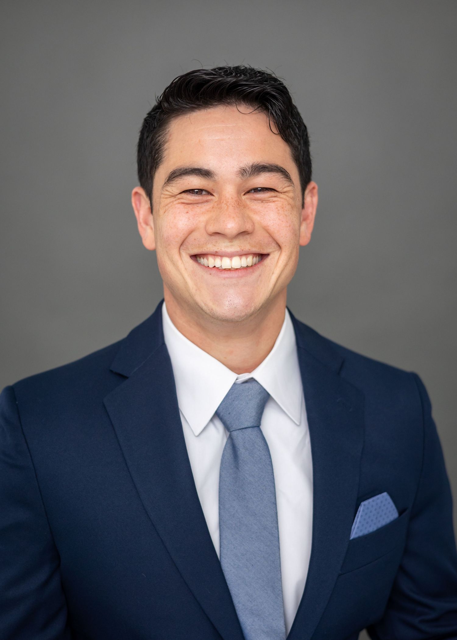 Professional headshot series showing expressions transitioning from subtle to broad smile in navy suit and tie.