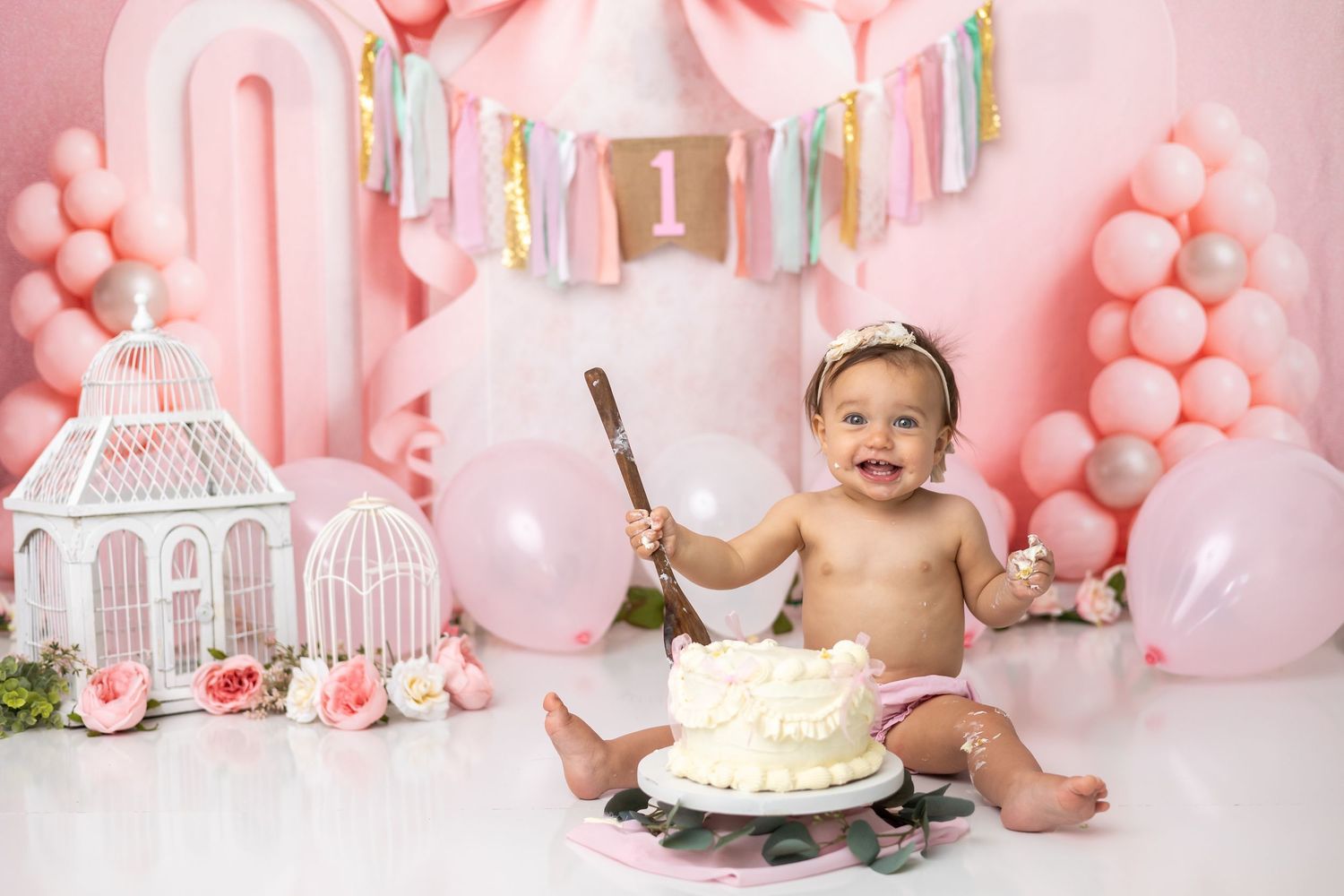 Baby girl celebrates first birthday smash cake session with pink balloons and decorations.