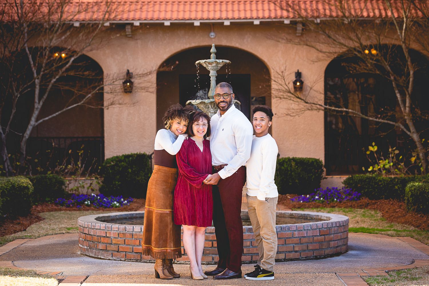 A group of four people stand together in front of a Spanish-style courtyard with a decorative fountain.
