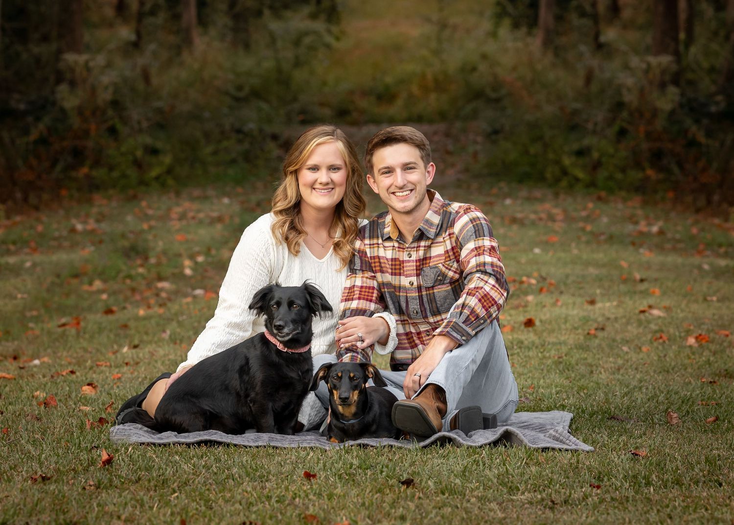 Couple relaxing on blanket outdoors with their black dog.
