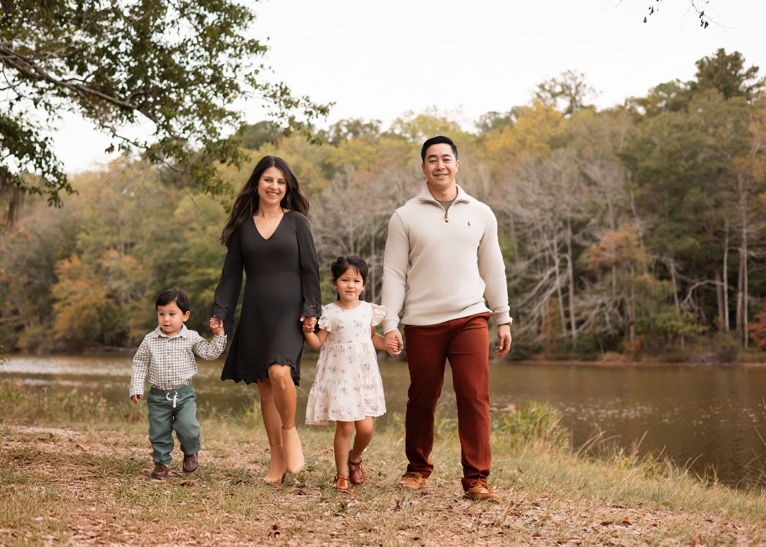 Family walking together along a scenic autumn path near a lake with fall foliage in the background.