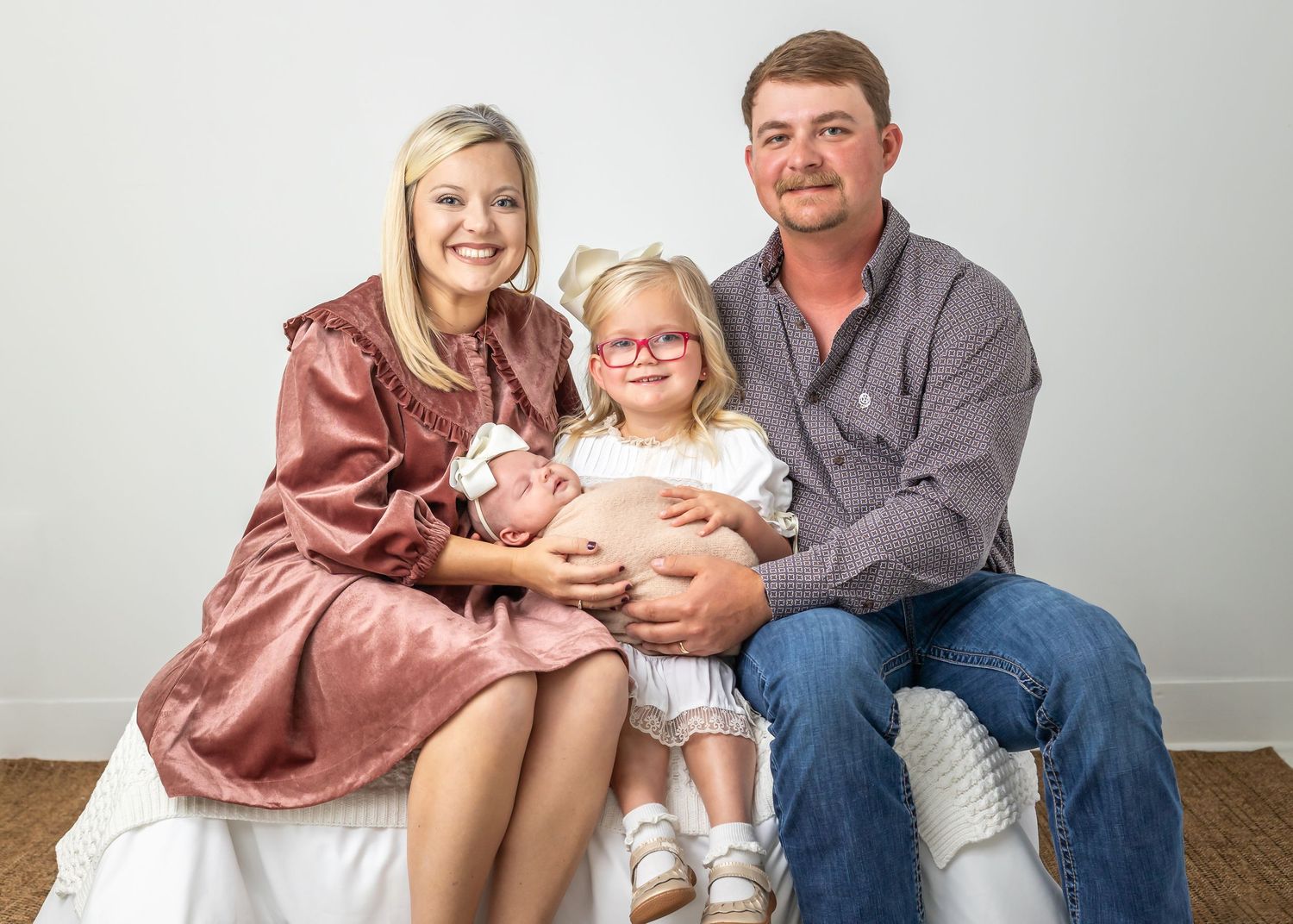 A family wearing coordinated outfits in pink and blue sits together on a white backdrop for a portrait session.