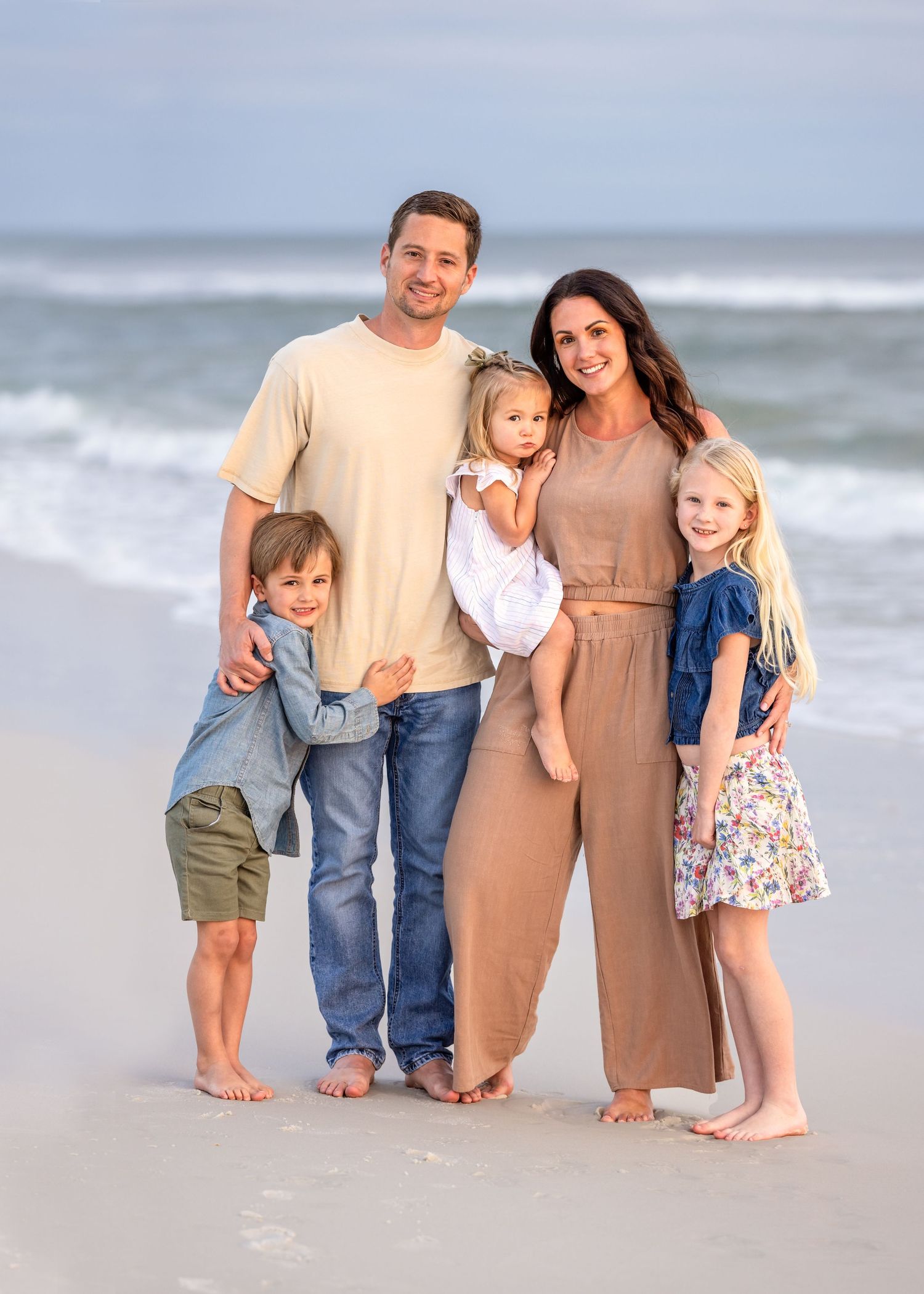Family walking together and posing for candid beach portraits at the ocean shore during sunset.