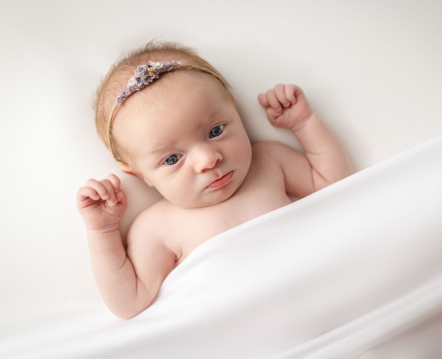 Sleeping newborn wearing delicate pink headband against white background.