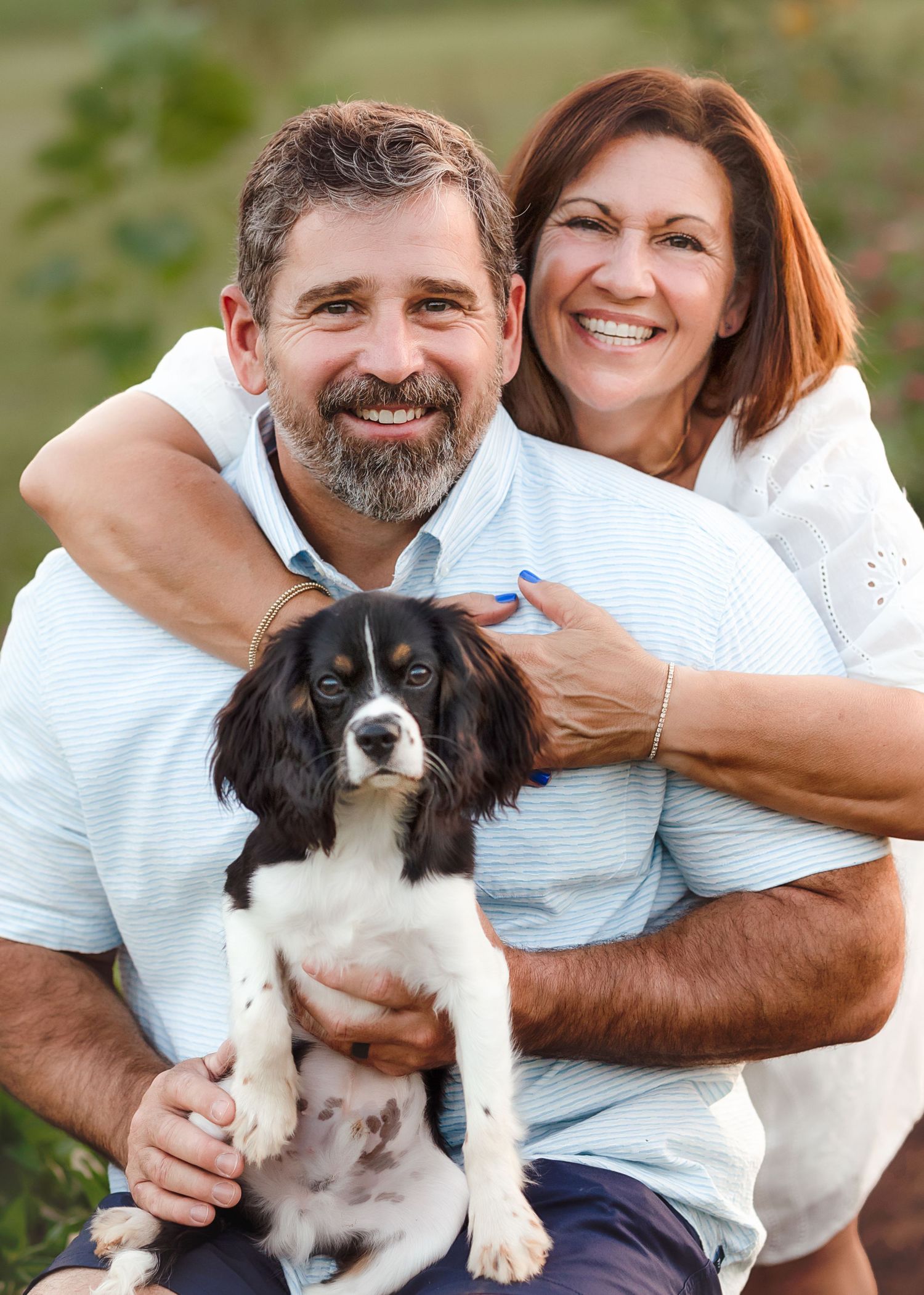 Happy couple poses with their black and white puppy in Alabama sunflower field.