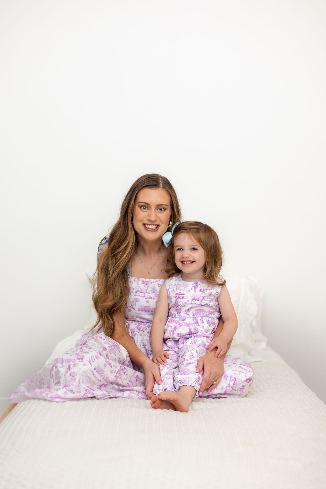 Mother and daughter wearing matching floral dresses pose together on white bedding.