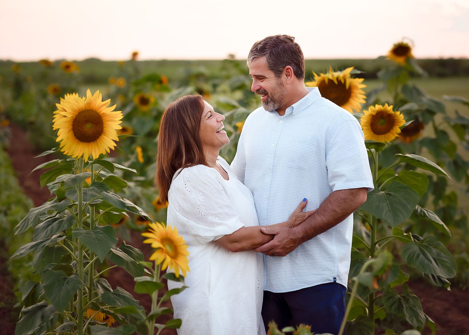 A couple shares a romantic moment in a vibrant sunflower field during a summer sunset photo session.