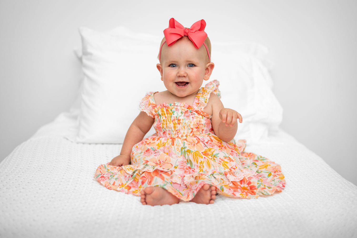 Baby wearing red bow headband and floral dress lying on white bedding in a series of adorable poses.