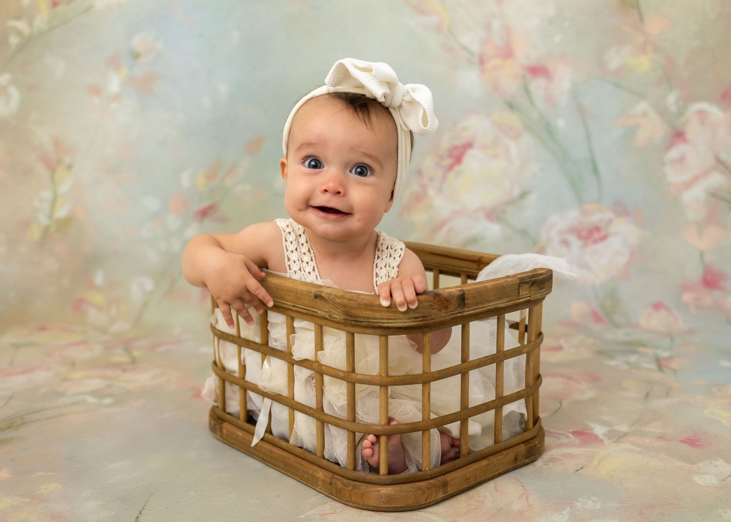 A baby sits in a wooden crate against a floral backdrop in a series of sweet portrait poses.