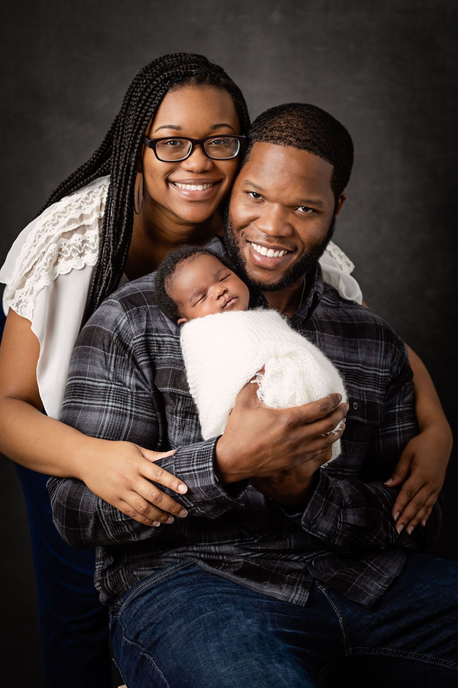 Couple cuddling with small white dog during intimate studio portrait session against dark background.