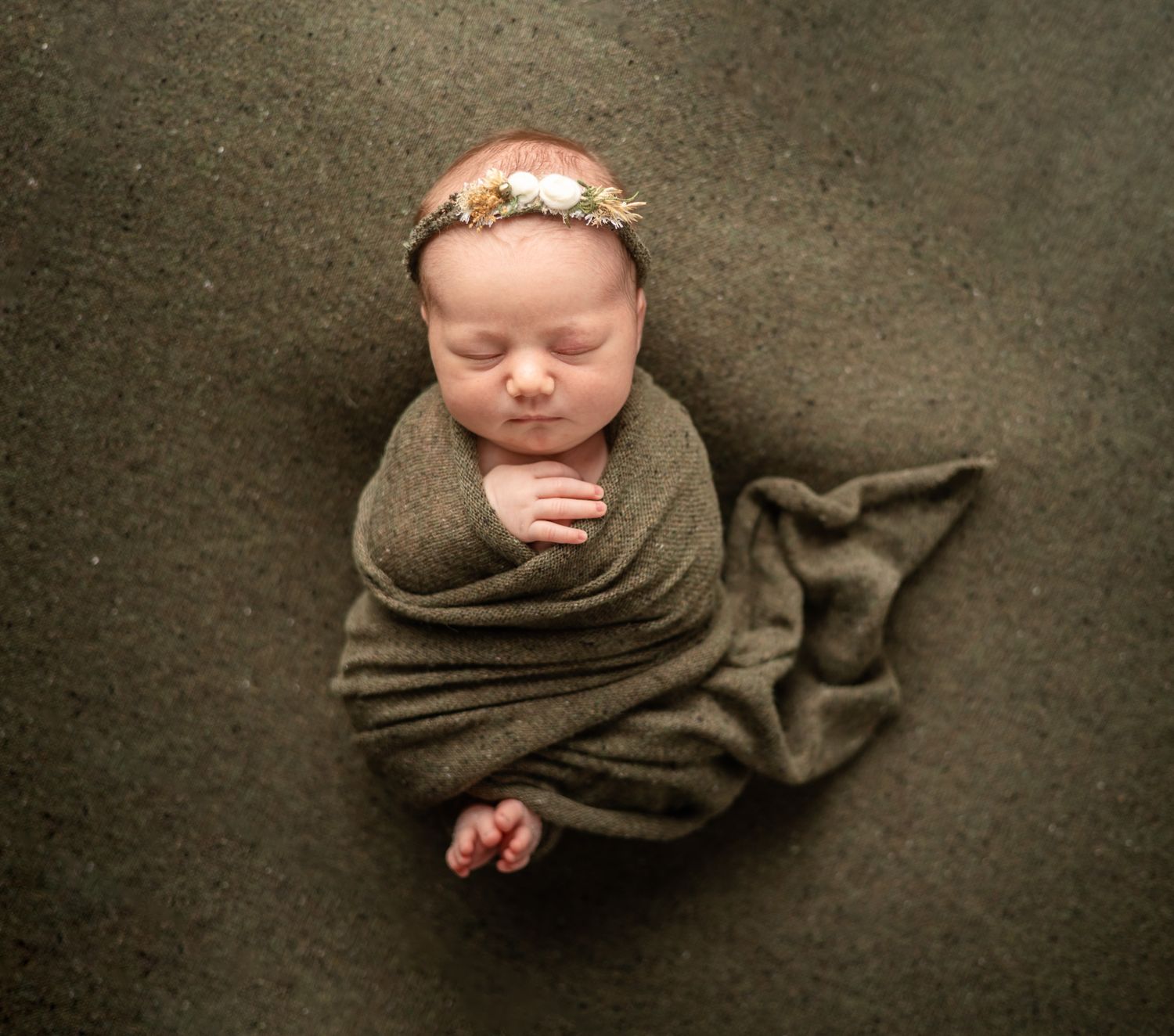 Sleeping newborn wrapped in brown fabric with floral headband in photography studio.