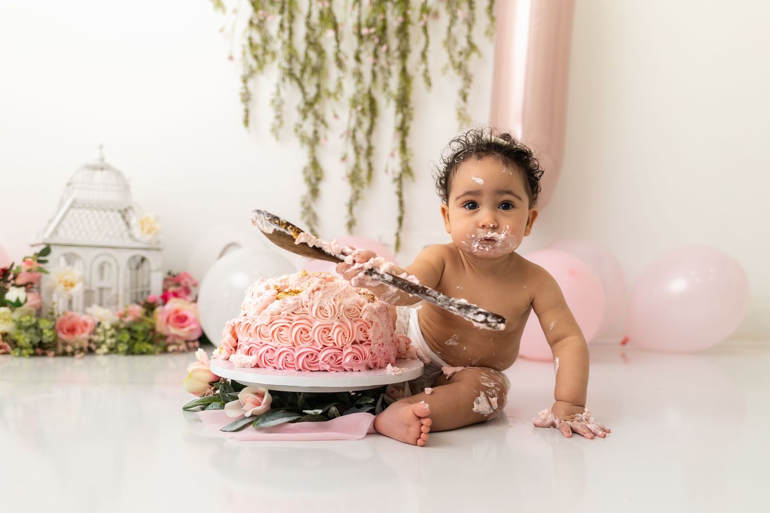 Baby girl smashing pink rosette first birthday cake during professional cake smash photo session.