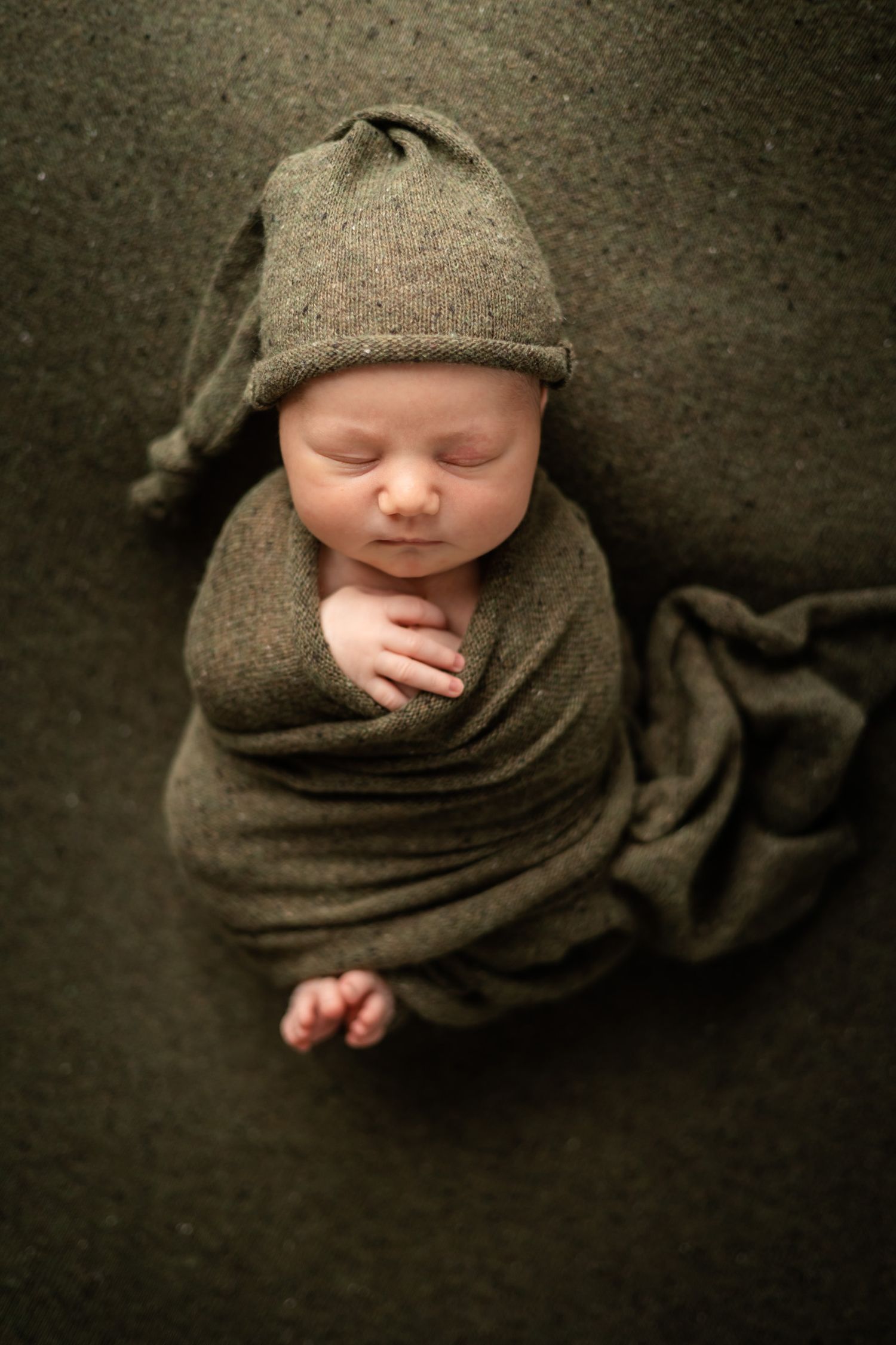 Newborn baby sleeping in gray wrap and knit hat on textured background.