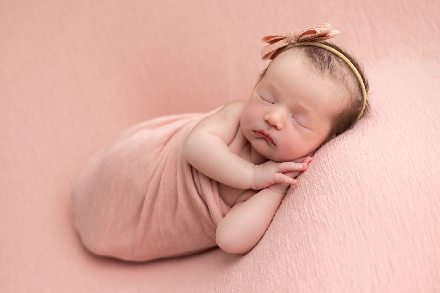 Peaceful sleeping newborn baby wrapped in soft pink swaddle blanket against pink background.