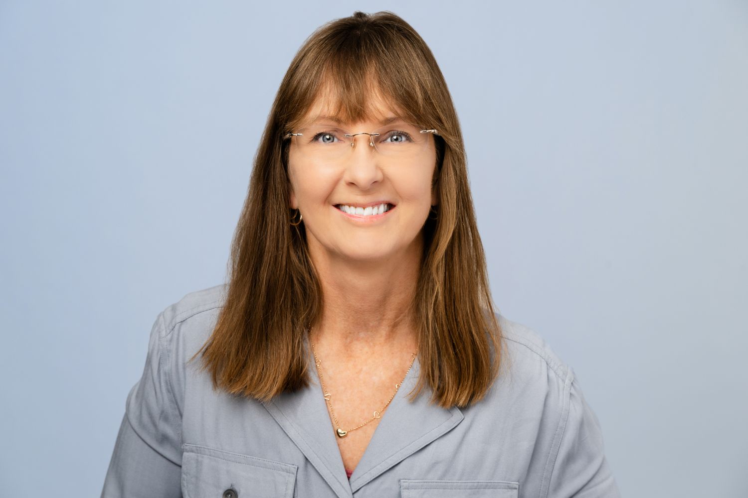 Professional headshot portrait of someone in a gray blazer smiling warmly against a light background.
