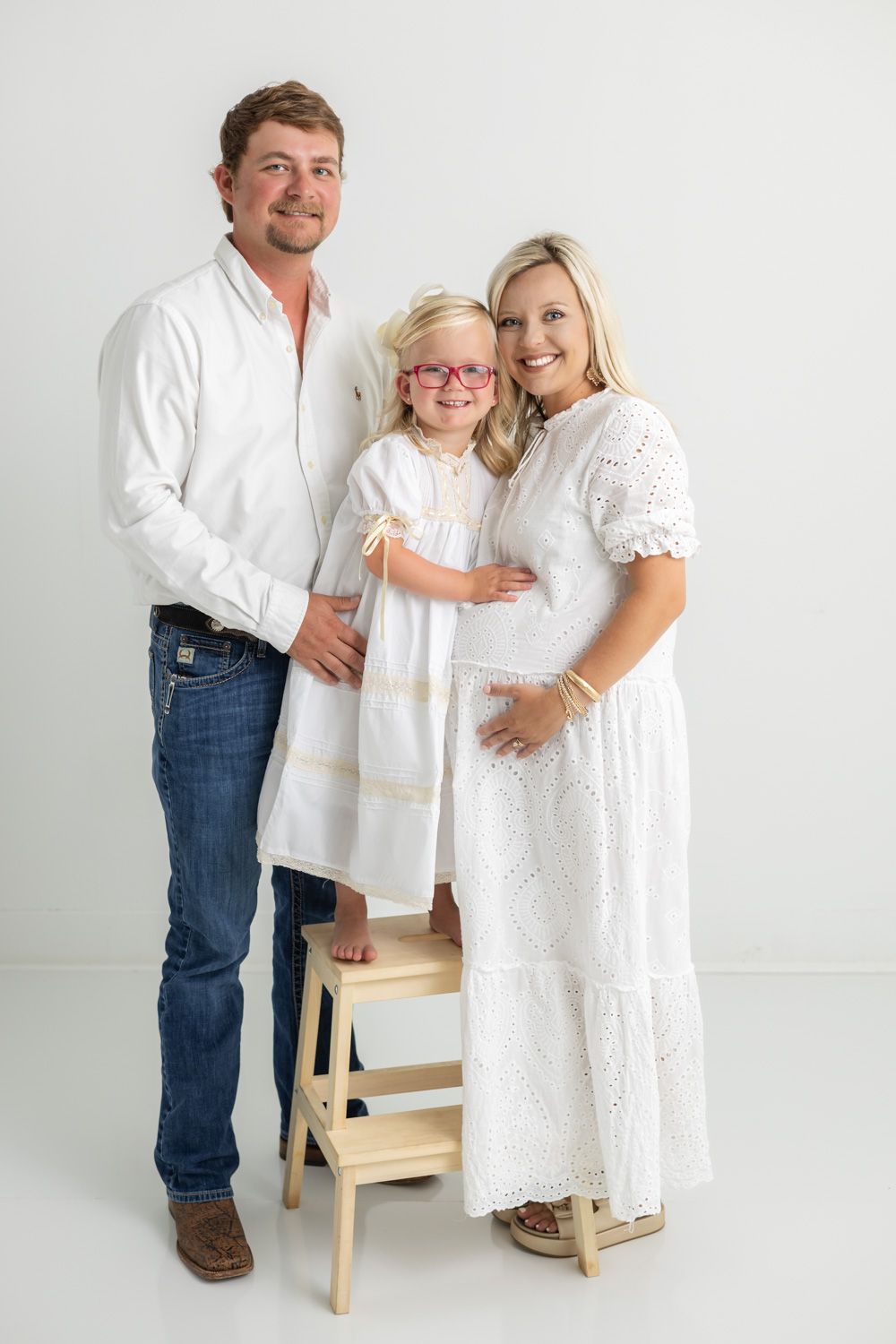 Family portrait in white outfits against clean studio background showing tender moments.