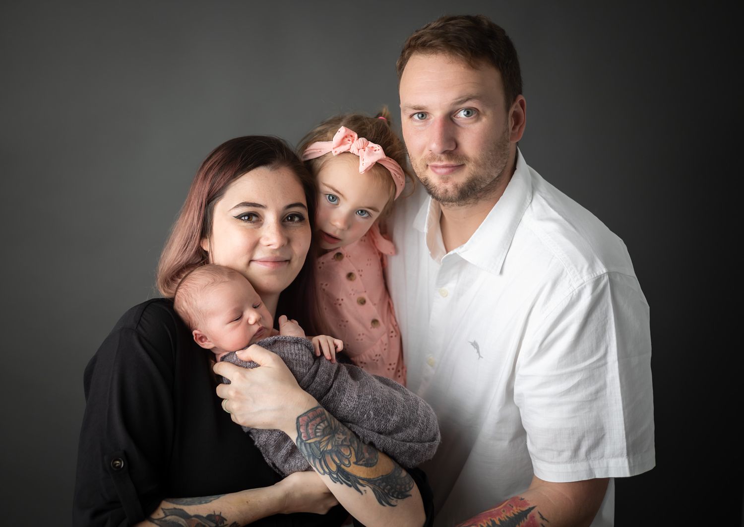 Family portrait with young child and baby against dark backdrop.