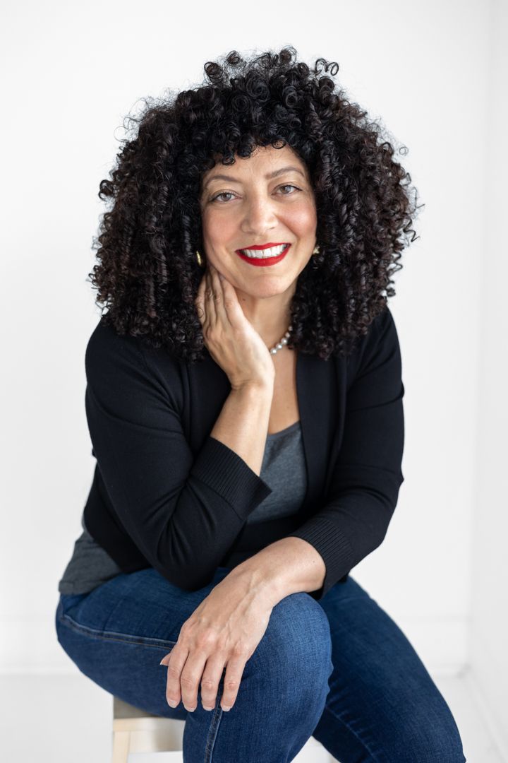 Professional studio portrait of someone wearing a black blazer and jeans while sitting casually against white background.