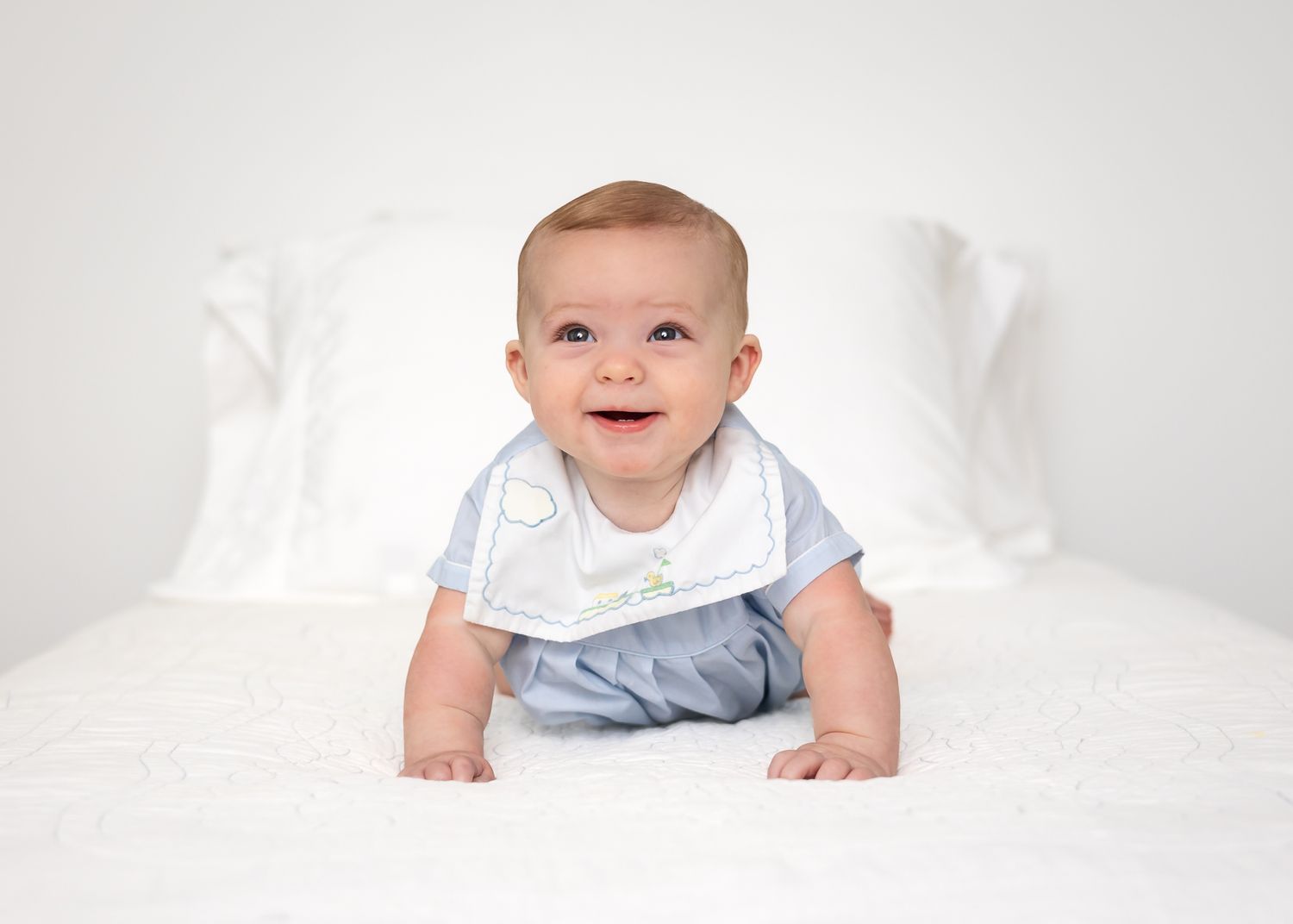 Baby in white outfit smiling on white background.