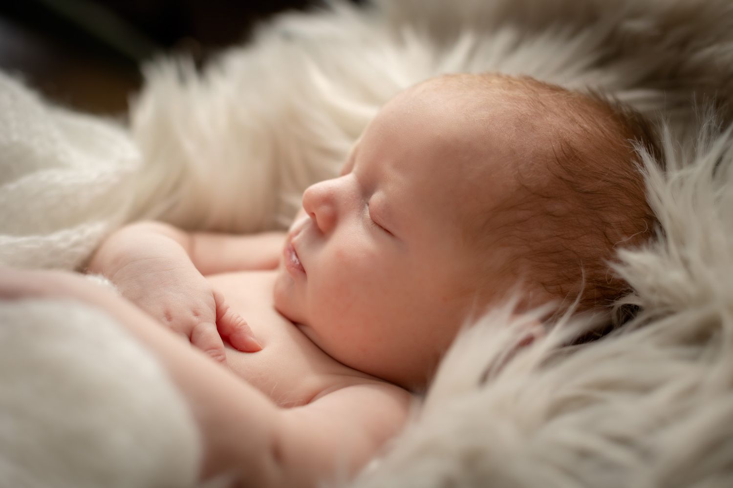Peaceful newborn sleeping on soft white fur blanket.