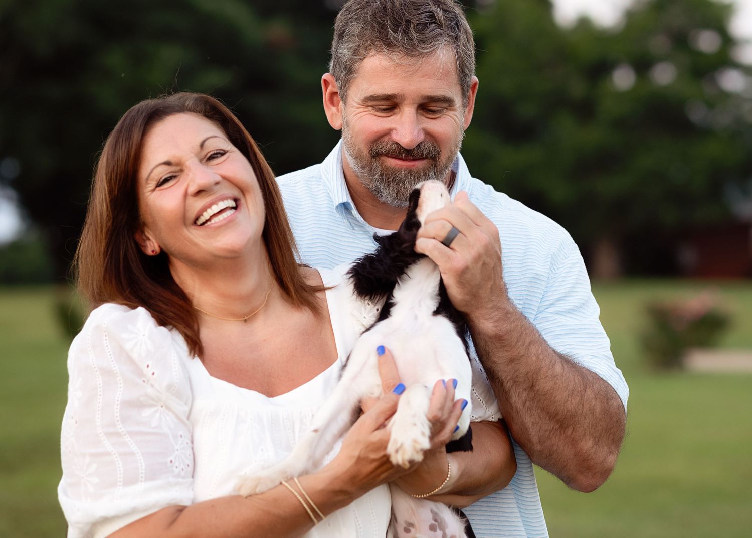 Playful couple shares candid moments with their puppy during outdoor photoshoot.