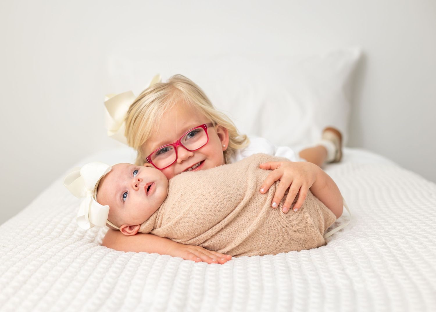 Two children cuddling together on white bedding.