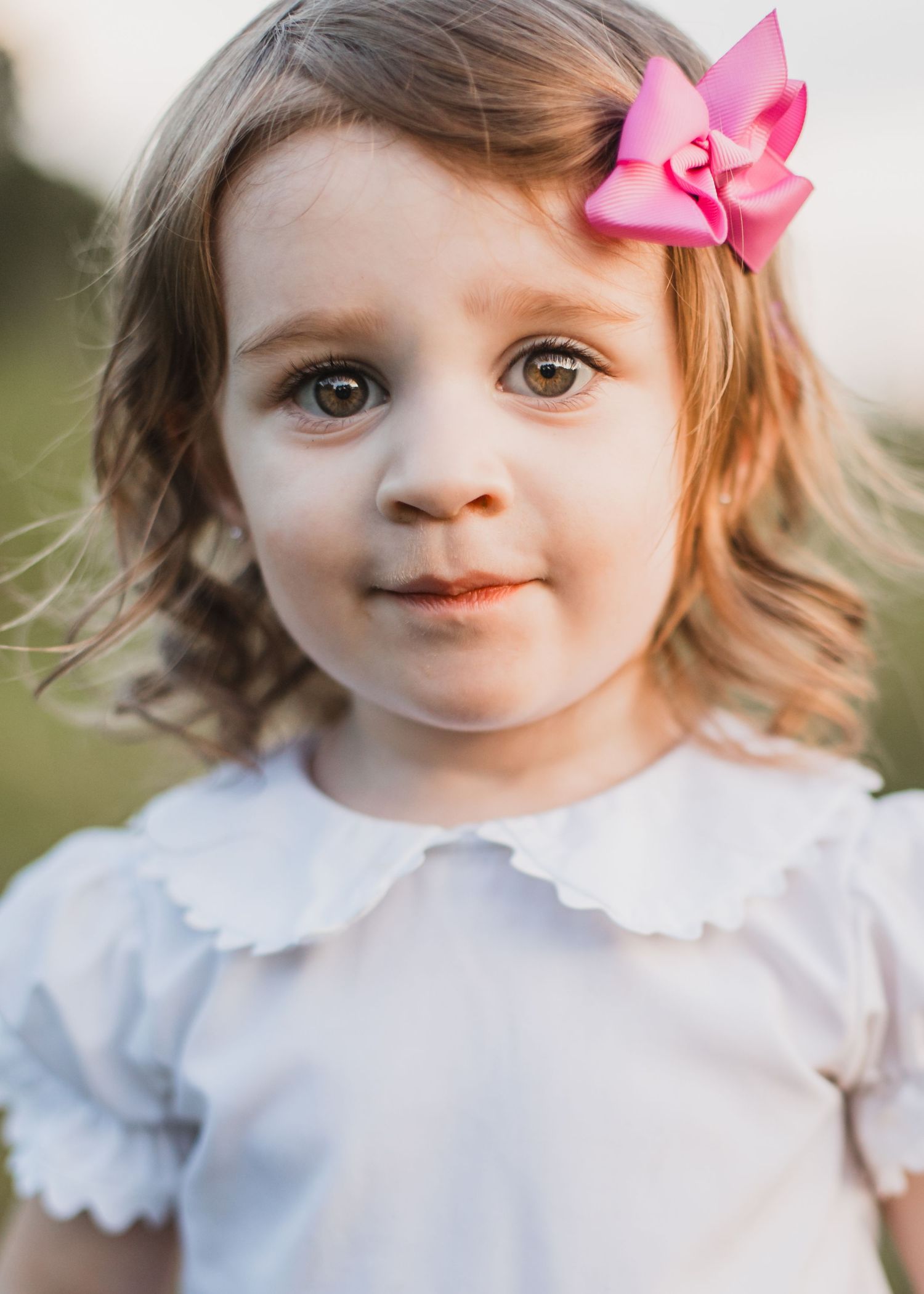 Young child in white dress with scalloped collar and pink bow.