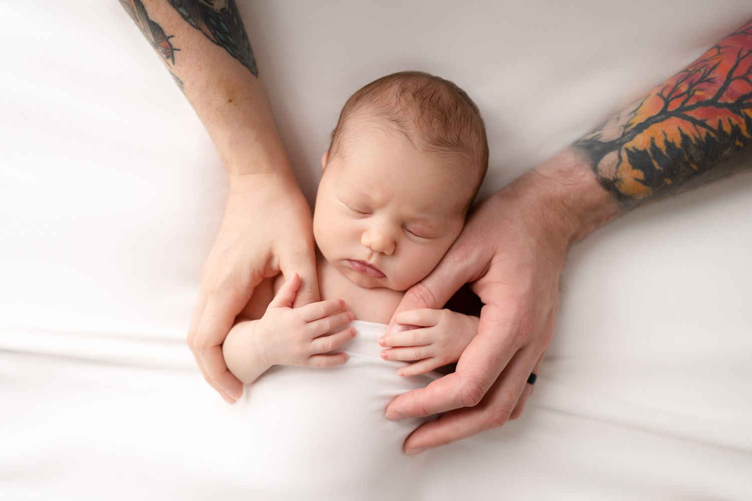 Close-up of sleeping newborn cradled in hands with tattoos.