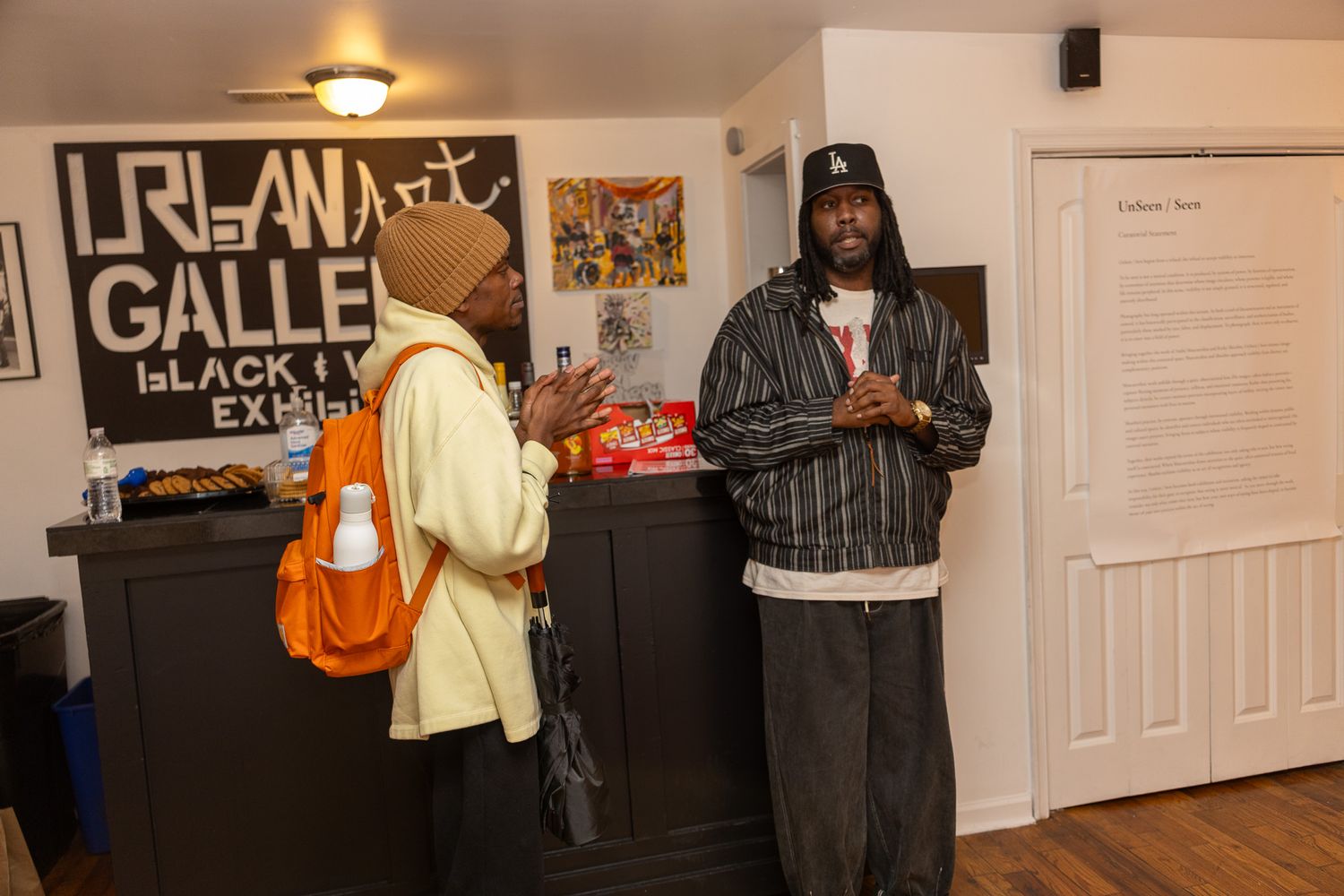 Two people conversing inside an urban art gallery featuring Black art exhibits and graffiti-style signage.