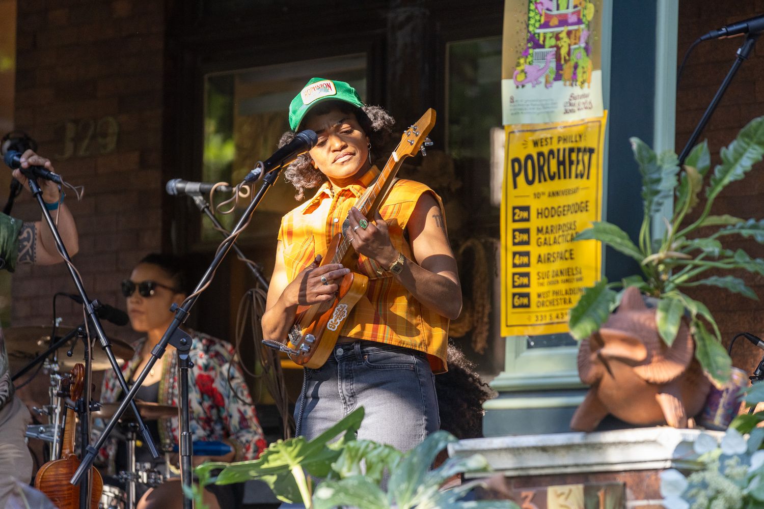 Musician playing ukulele on a porch at an outdoor Porchfest music festival on a sunny day.