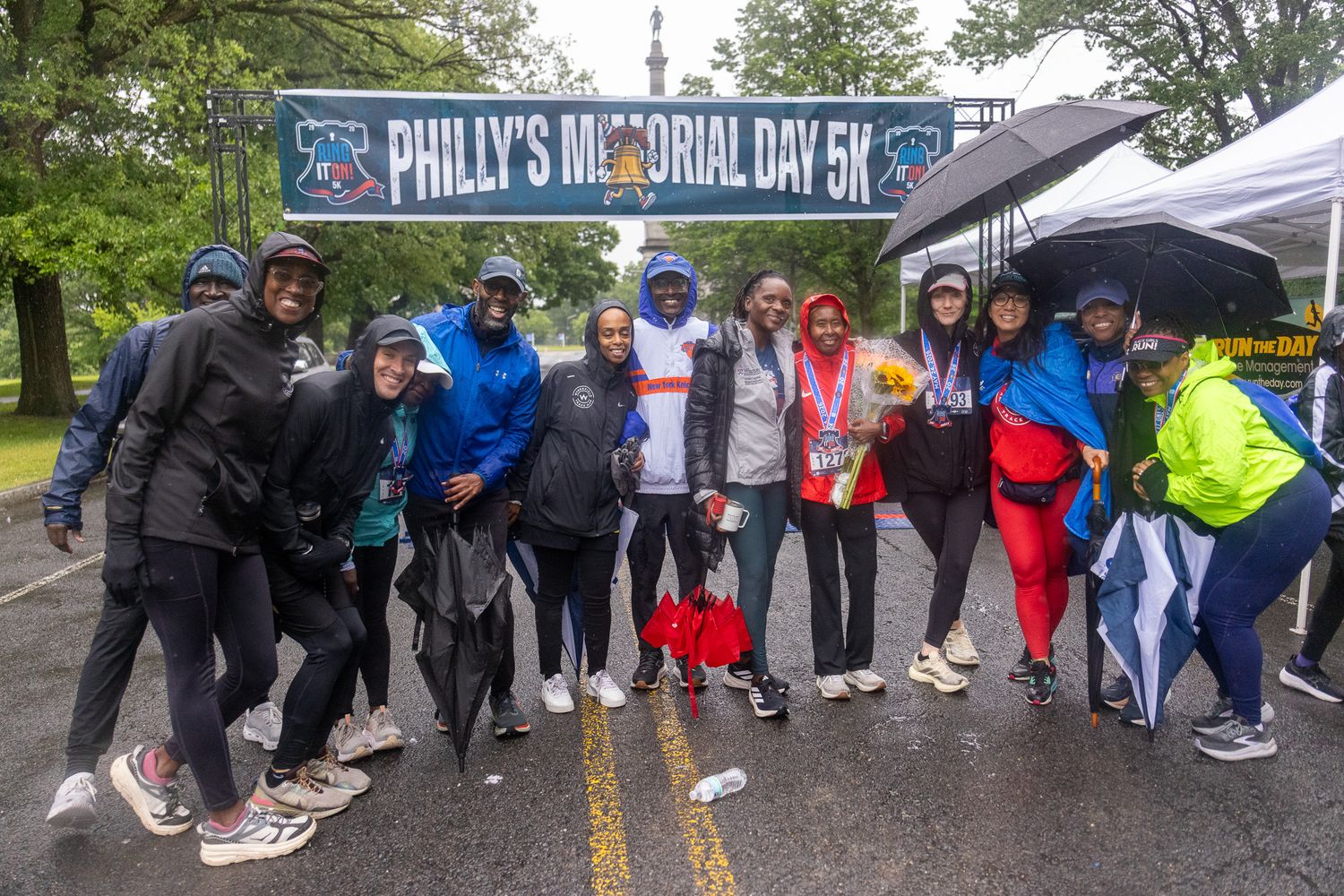 Group of runners posing under Philly's Memorial Day 5K banner on a rainy day in Philadelphia.
