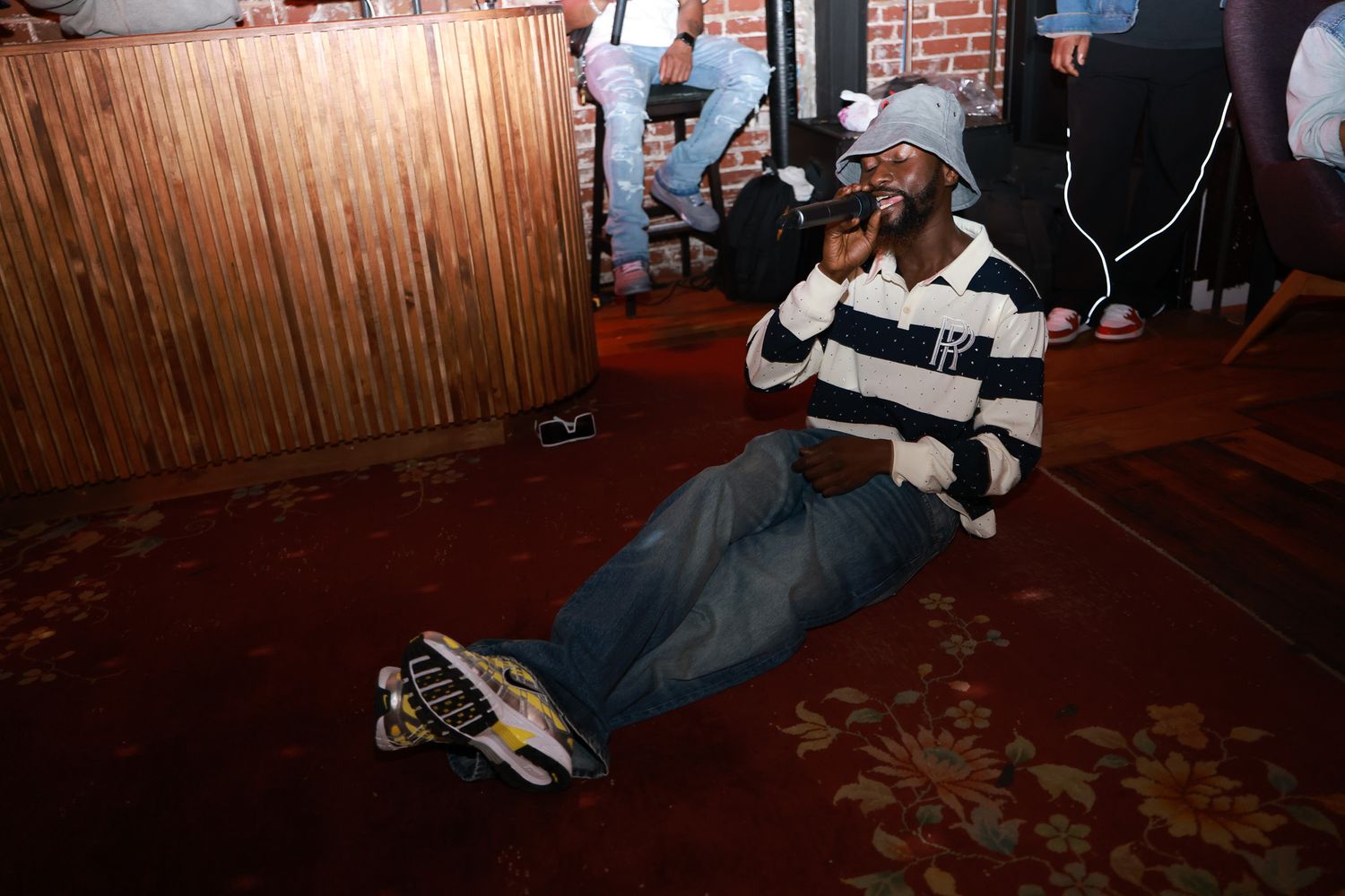A group of people sit together in a dimly lit room with brick walls and wooden panels during an indoor gathering.