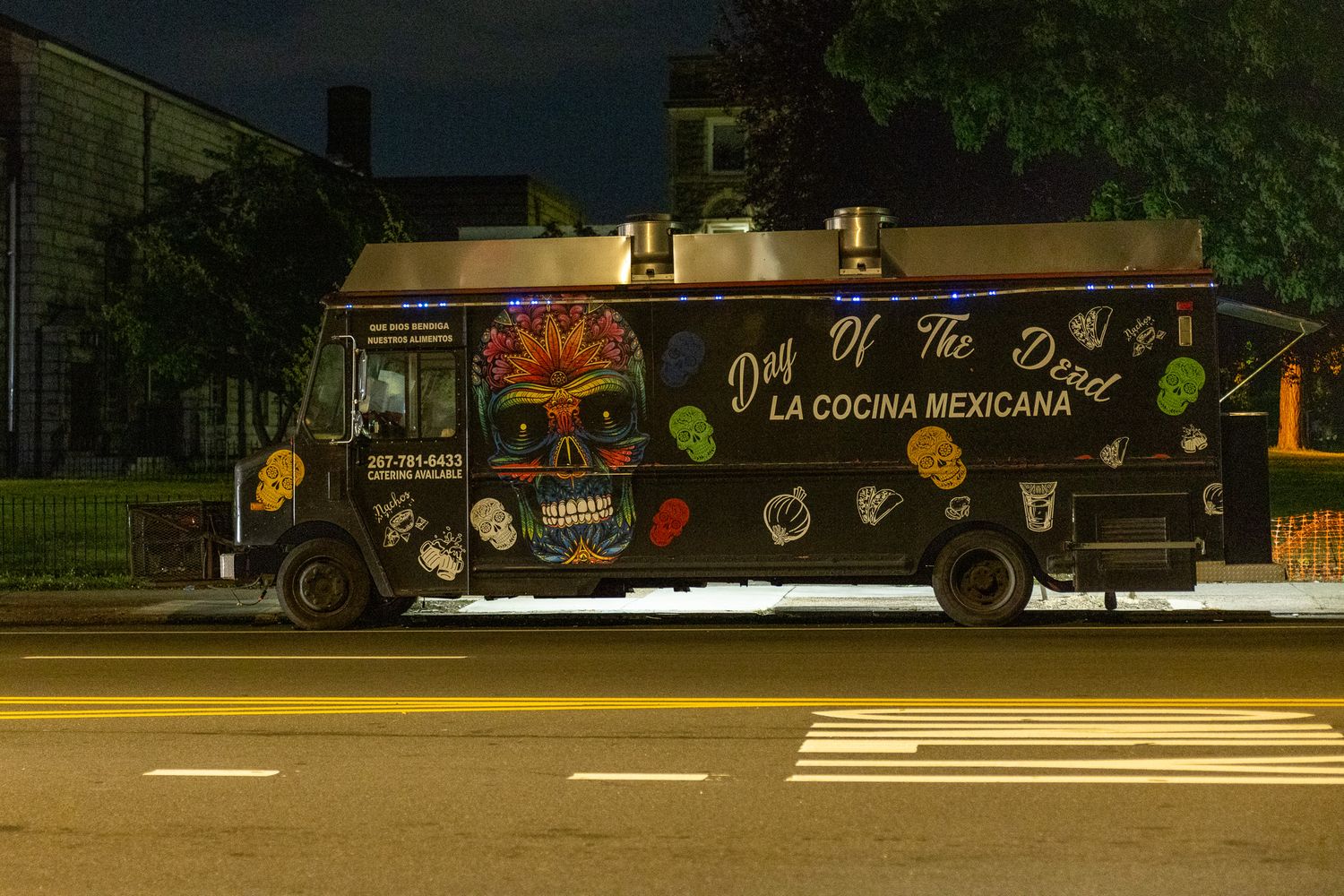Day of the Dead Mexican food truck parked on a city street at night with colorful skull artwork.