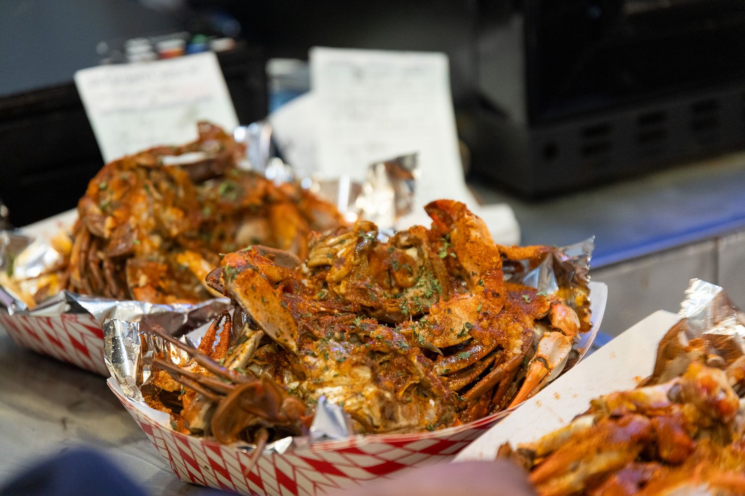 Seasoned cooked crabs served in red and white checkered paper-lined baskets at a seafood food stall.