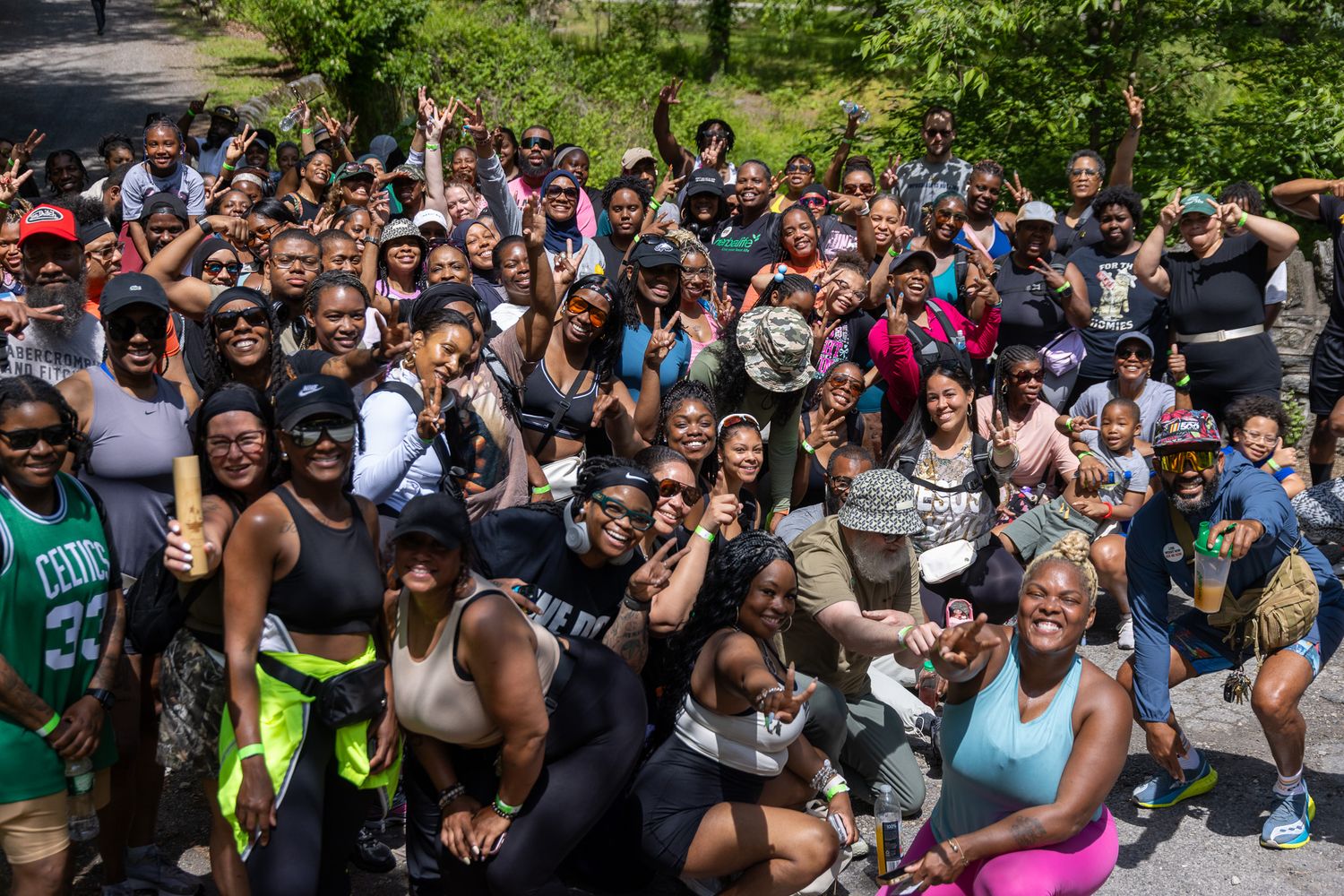 Large diverse group of smiling people posing outdoors in athletic wear during a community fitness event in a park.