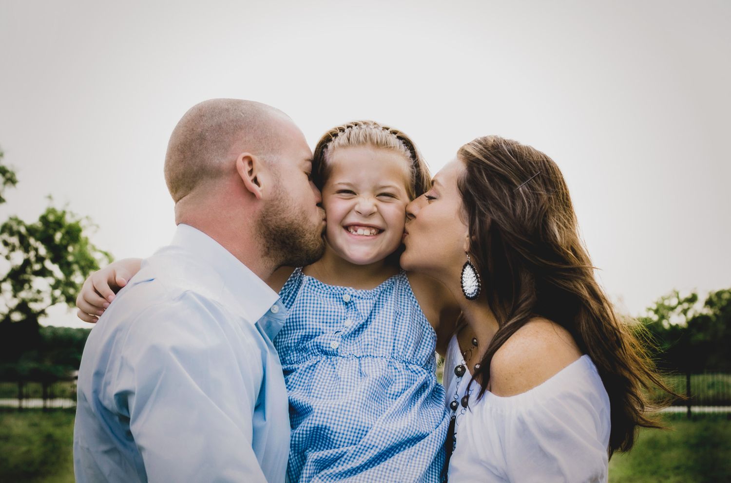 Mom and Dad kissing daughter's cheeks in a outdoor family portrait, natural light photography, Finger Lakes NY, Soft Wild Light.