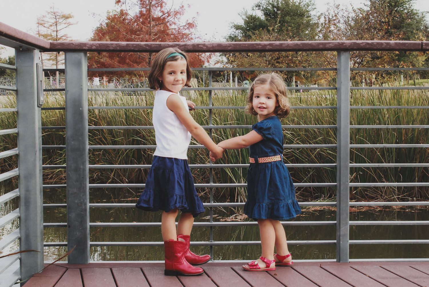 Two young children holding hands on a bridge surrounded by autumn foliage, sibling portraits, Finger Lakes NY