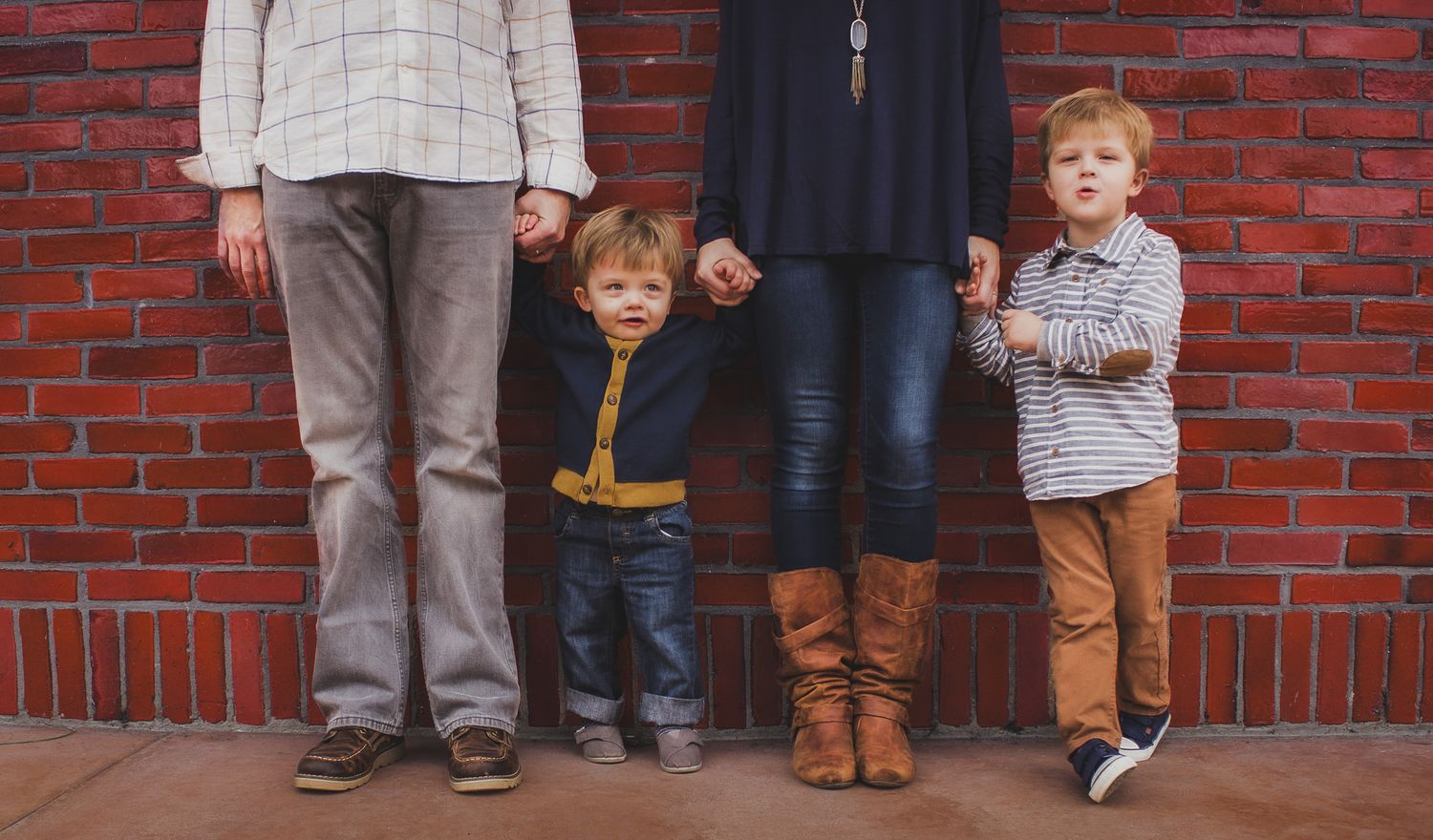 Family of four holding hands against a red brick wall, outdoor family portrait, Finger Lakes NY, Soft Wild Light.