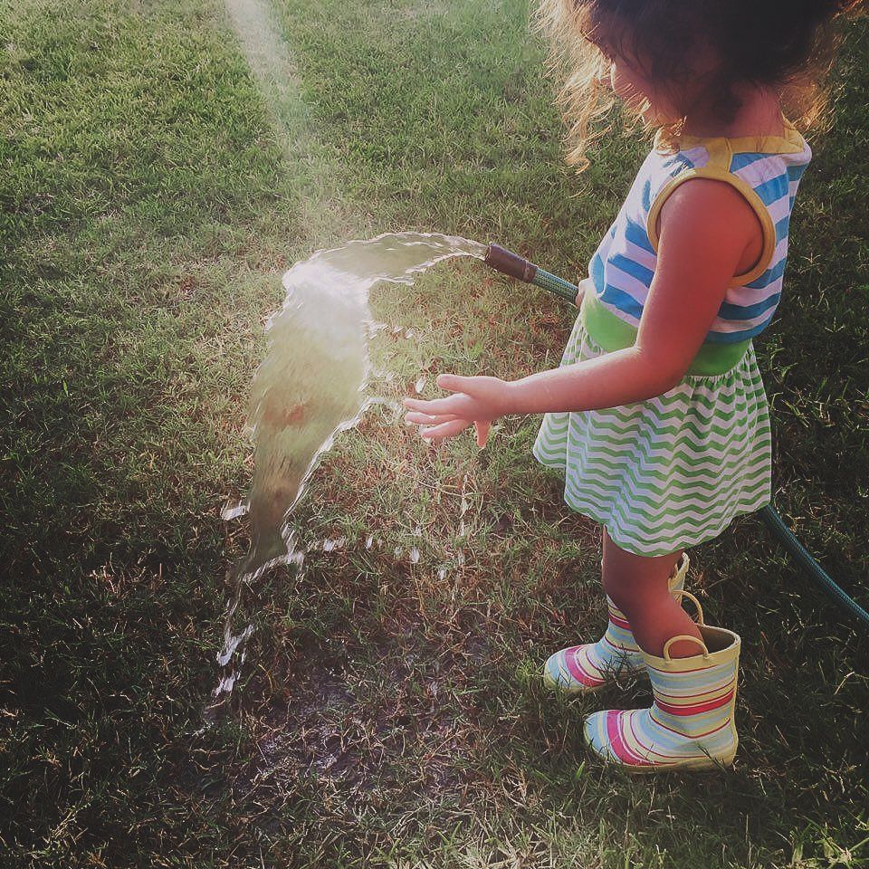 Young child playing outdoors with a water hose in bright sunlight, candid natural light portrait, Finger Lakes New York, Soft Wild Light.
